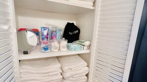 A white closet with shelves holding folded towels, a black hair dryer, cotton balls, and a mirror. - “Up in the hill” is a charming, 1 bedroom apartment located in Haines City (Haines City)