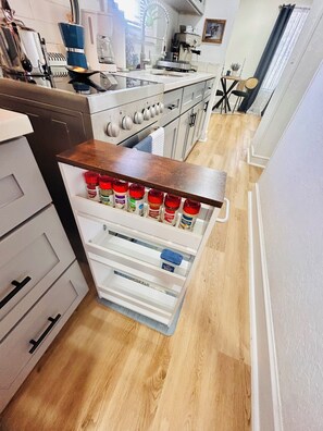 A kitchen with a built-in spice rack, a coffee machine, and a window with curtains.