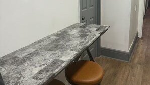 Un couloir avec une table en marbre et deux tabourets en cuir marron, une porte grise et un tableau encadré au mur.