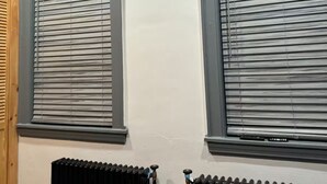 Deux fenêtres équipées de stores horizontaux, un radiateur et une porte en bois.