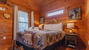 Een houten slaapkamer met een bed, twee nachtkastjes, een raam en een lijst met een afbeelding aan de muur.