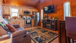Een knus interieur in chaletstijl met houten wanden, een keuken met moderne apparatuur, een comfortabele zithoek en een wandgemonteerde flatscreen-tv.