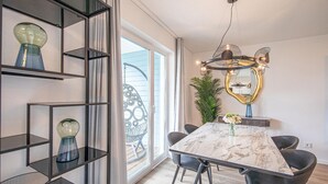 Un comedor moderno con una mesa de mármol, sillas oscuras, un espejo decorativo y un ventanal con vistas.