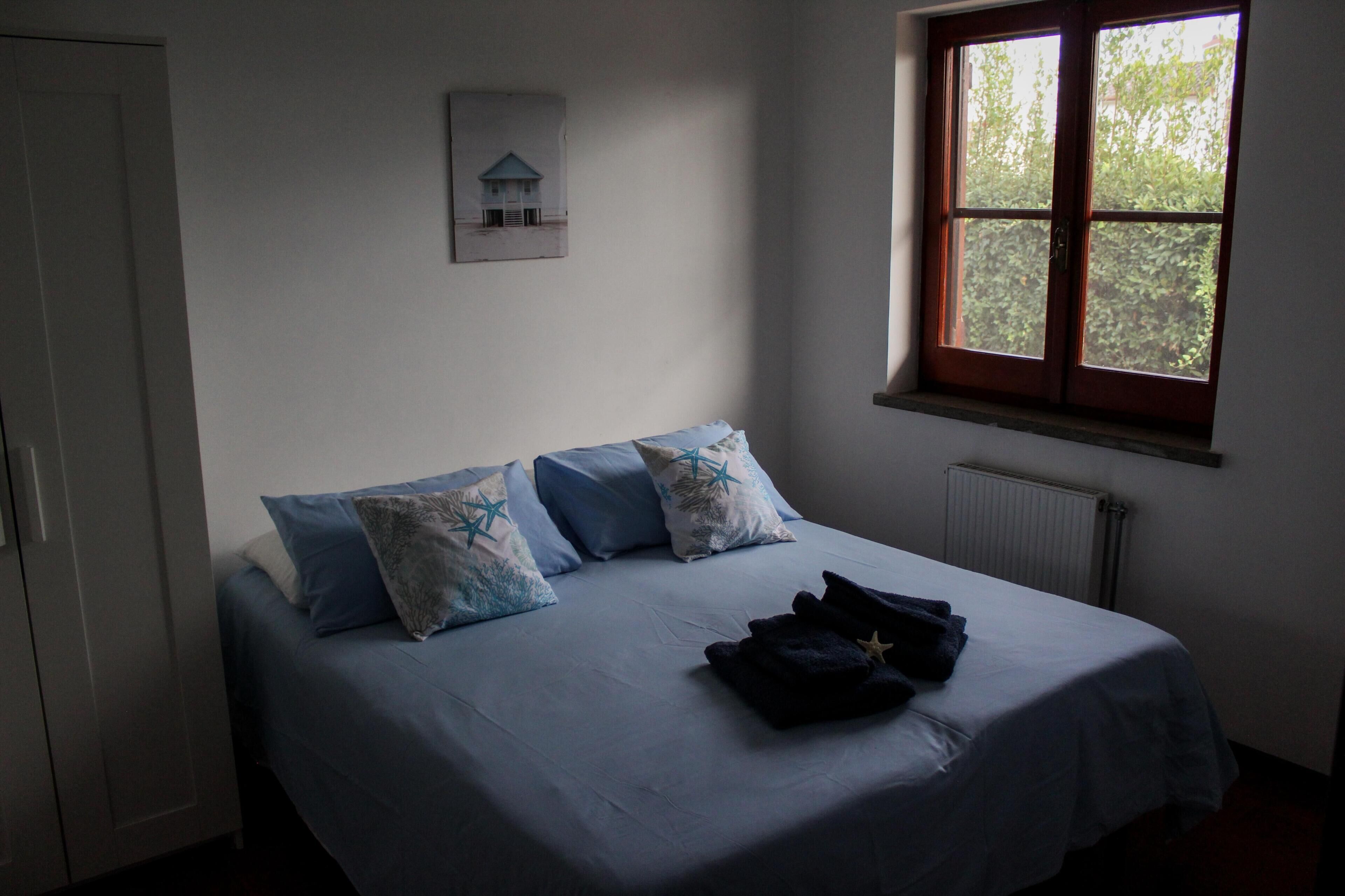 A bedroom with a bed, pillows, a window, and a radiator.
