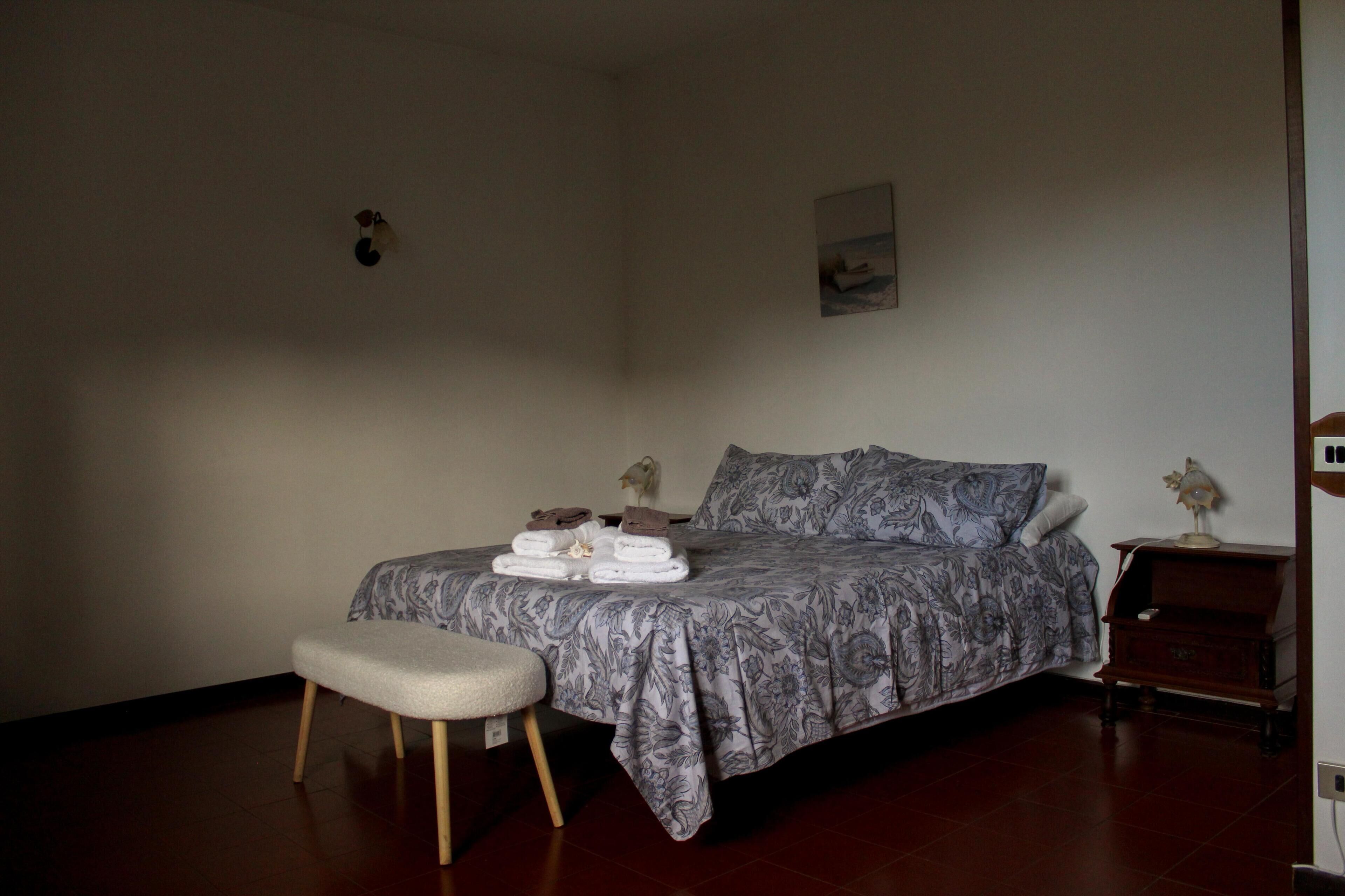 A bedroom with a bed, a bedside table, a nightstand, a chair, and a wall-mounted lamp.