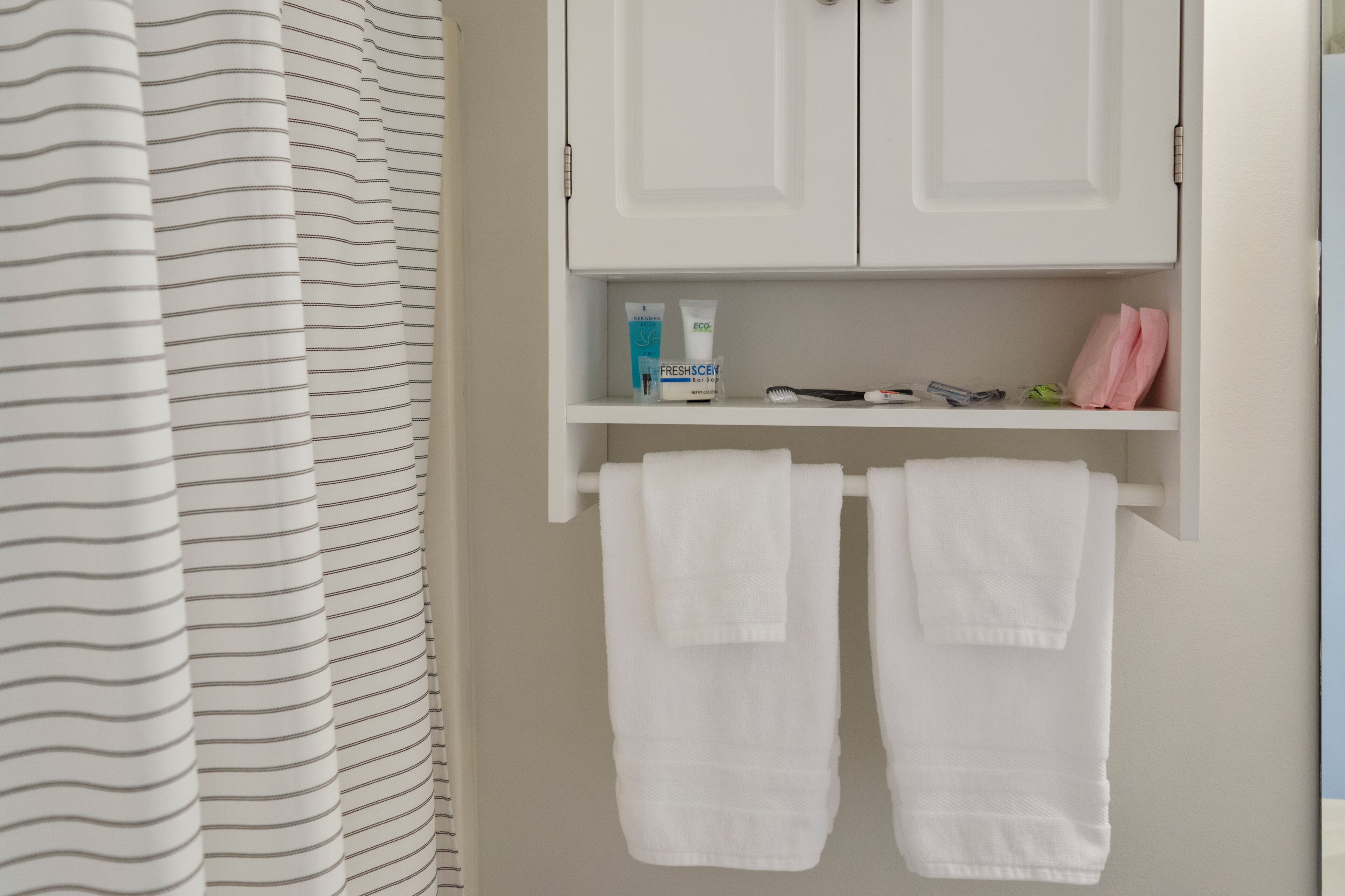 Un bagno con tende a righe, un portasciugamani bianco con due asciugamani, uno scaffale con articoli da toilette e un armadietto.
