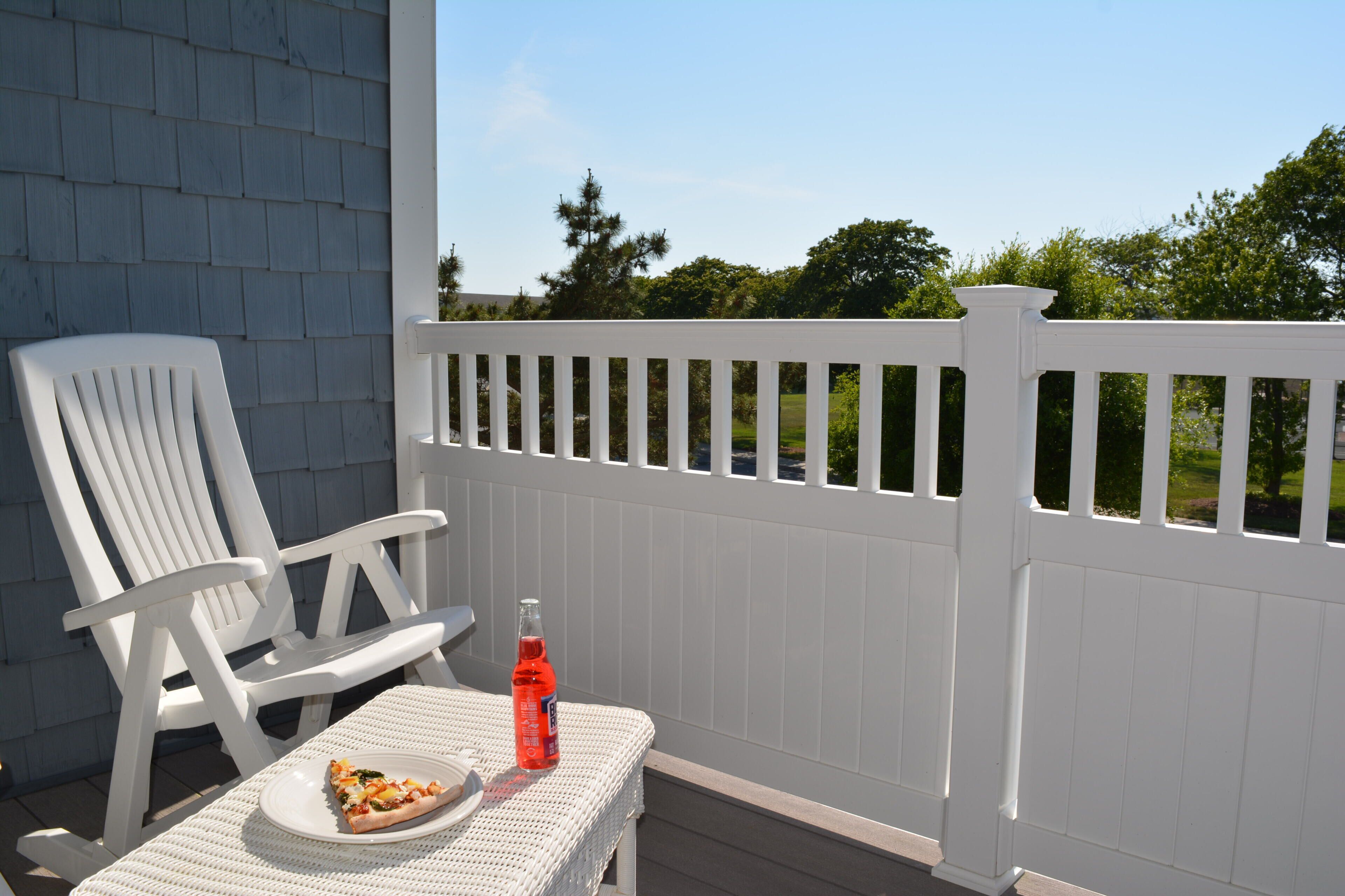 En hvid dækket terrasse med en hvid stol og et bord, et pizzastykke og en sodavandsflaske.