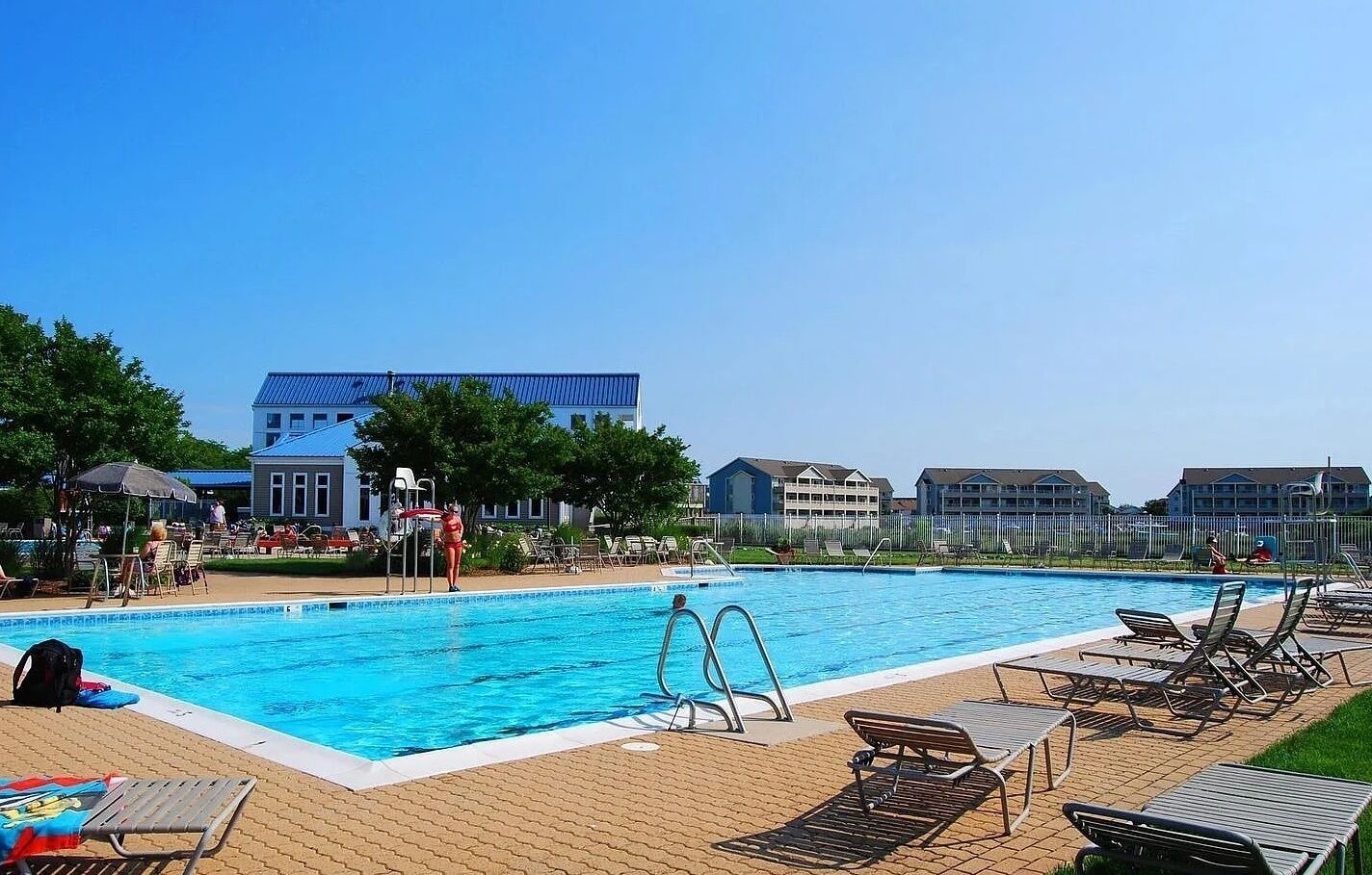 Piscina com espreguiçadeiras e um edifício ao fundo.
