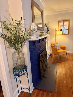 A living room with a fireplace, a mirror, a sofa, and a decorative plant. - Newly Remodeled Mid-Century Bungalow in Western North Carolina's Best Small Town (Hendersonville)