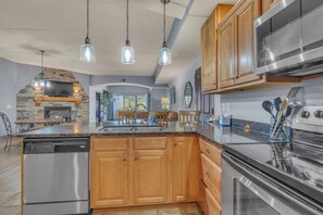A modern kitchen with granite countertops, stainless steel appliances, wooden cabinets, and pendant lighting. - High Tides - Sleeps 14 | Video Games (Wisconsin Dells)