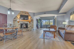 A spacious living room with a stone fireplace, a dining area with a metal chair, and a sofa. - High Tides - Sleeps 14 | Video Games (Wisconsin Dells)