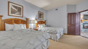 A hotel room with two beds, a wooden headboard, a nightstand, a lamp, and a fireplace.