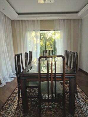 A dining area with a glass-top table surrounded by chairs, a patterned rug, and sheer curtains.
