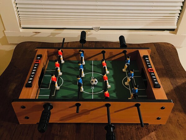 Una mesa de fútbol de mesa con un balón de fútbol en el centro, rodeada por jugadores con camisetas rojas y azules.