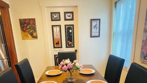 A dining table with six chairs, a vase with flowers, and framed artwork on the wall.