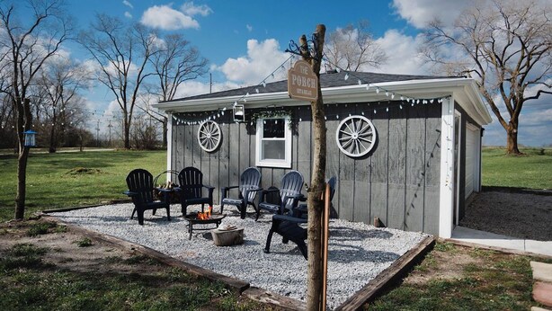 Una pequeña cabaña de madera con un porche, mobiliario exterior y un letrero que dice 'The Porch'.