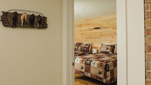 Un dormitorio con suelo de madera, una cama con colcha estampada y una decoración de caballo montado en la pared.