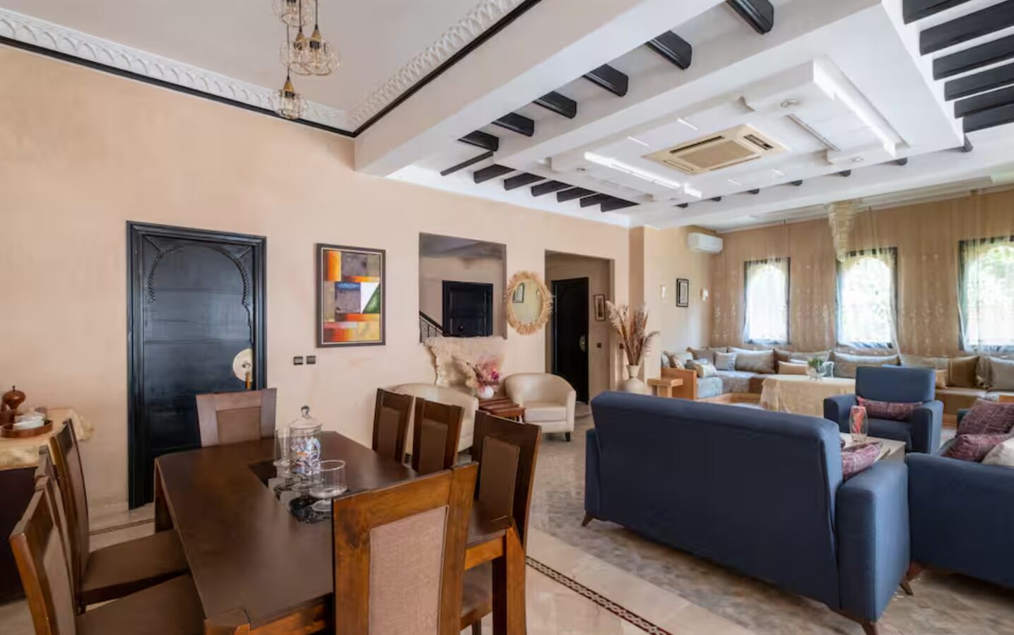 A dining area with a wooden table and chairs, a living room with a blue sofa, and a staircase leading to another level.
