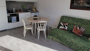 A modern kitchen with white cabinets, a dining table with chairs, and a green sofa with patterned cushions. - 247 - Your stay facing Hourtin Port – Superb view and peaceful setting (HOURTIN)