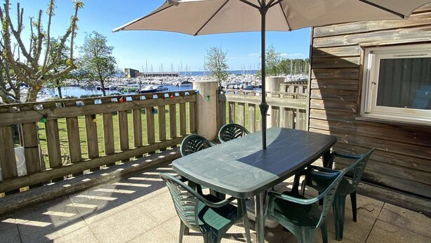 An outdoor patio with a table and chairs, an umbrella, and a view of boats in the background. - 247 - Your stay facing Hourtin Port – Superb view and peaceful setting (HOURTIN)