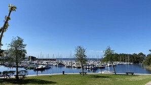 A marina with boats docked, a grassy area with benches, and a clear blue sky. - 247 - Your stay facing Hourtin Port – Superb view and peaceful setting (HOURTIN)