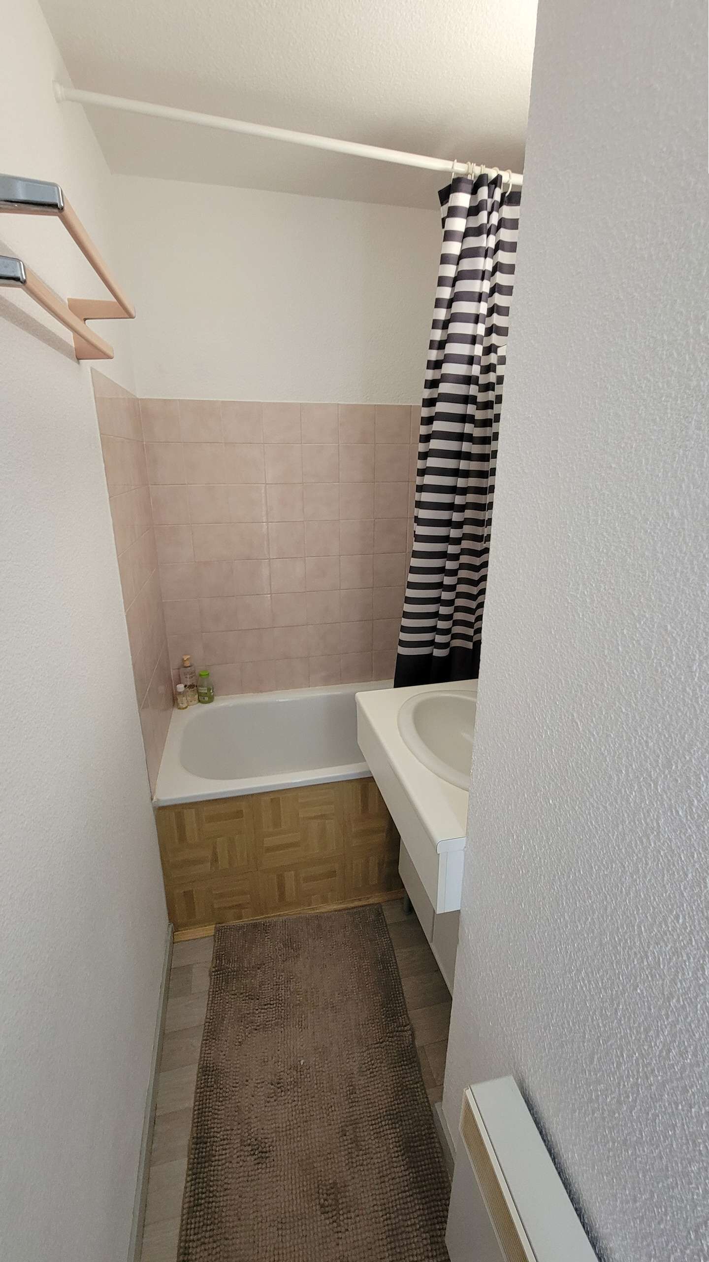 A small bathroom with a bathtub, a shower curtain, a towel rack, and a rug.
