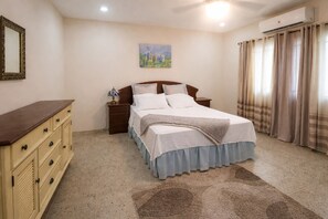 A bedroom with a bed, nightstands, a dresser, a painting, and a window with curtains.