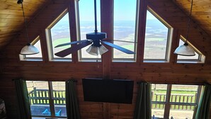 Une pièce dotée d’un plafond en pente, de grandes fenêtres, d’un ventilateur de plafond et d’un téléviseur à écran plat.