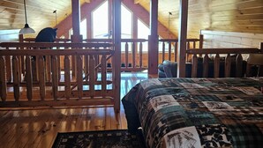 Un intérieur en bois avec un lit, une rambarde en bois et une vue sur l’extérieur.