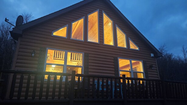Une cabane en rondins dotée de grandes fenêtres, d’une terrasse et d’une antenne parabolique.