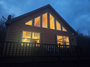 A log cabin with large windows, a deck, and a satellite dish.