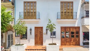 A two-story building with a white facade, wooden doors, and balconies.