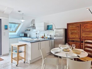A modern kitchen with white cabinets, a built-in oven, and a dining area with a round table set for four. - Carnac – 3-room apartment – 65m² – Wi-Fi (CARNAC)