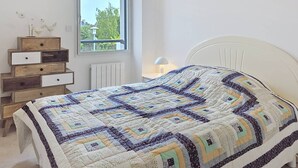 Ein Schlafzimmer mit Bett, Kommode mit Schubladen, Fenster und Heizkörper.