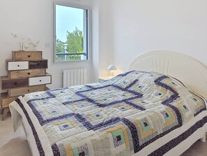 A bedroom with a bed, a dresser with drawers, a window, and a radiator. - Carnac – 3-room apartment – 65m² – Wi-Fi (CARNAC)