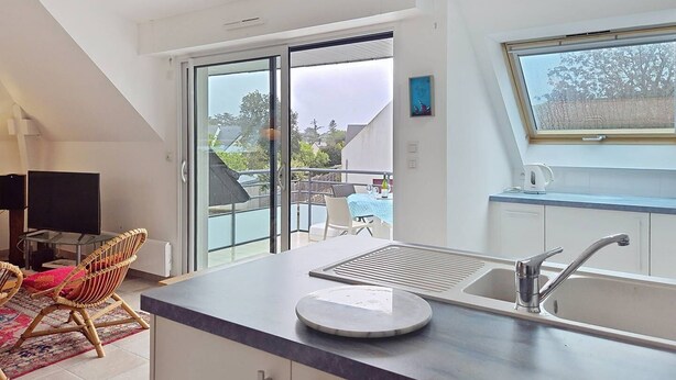 Eine moderne Küche mit einem großen Fenster, eine Essecke mit Tisch und Stühlen sowie ein Balkon mit Blick auf die Nachbarschaft.