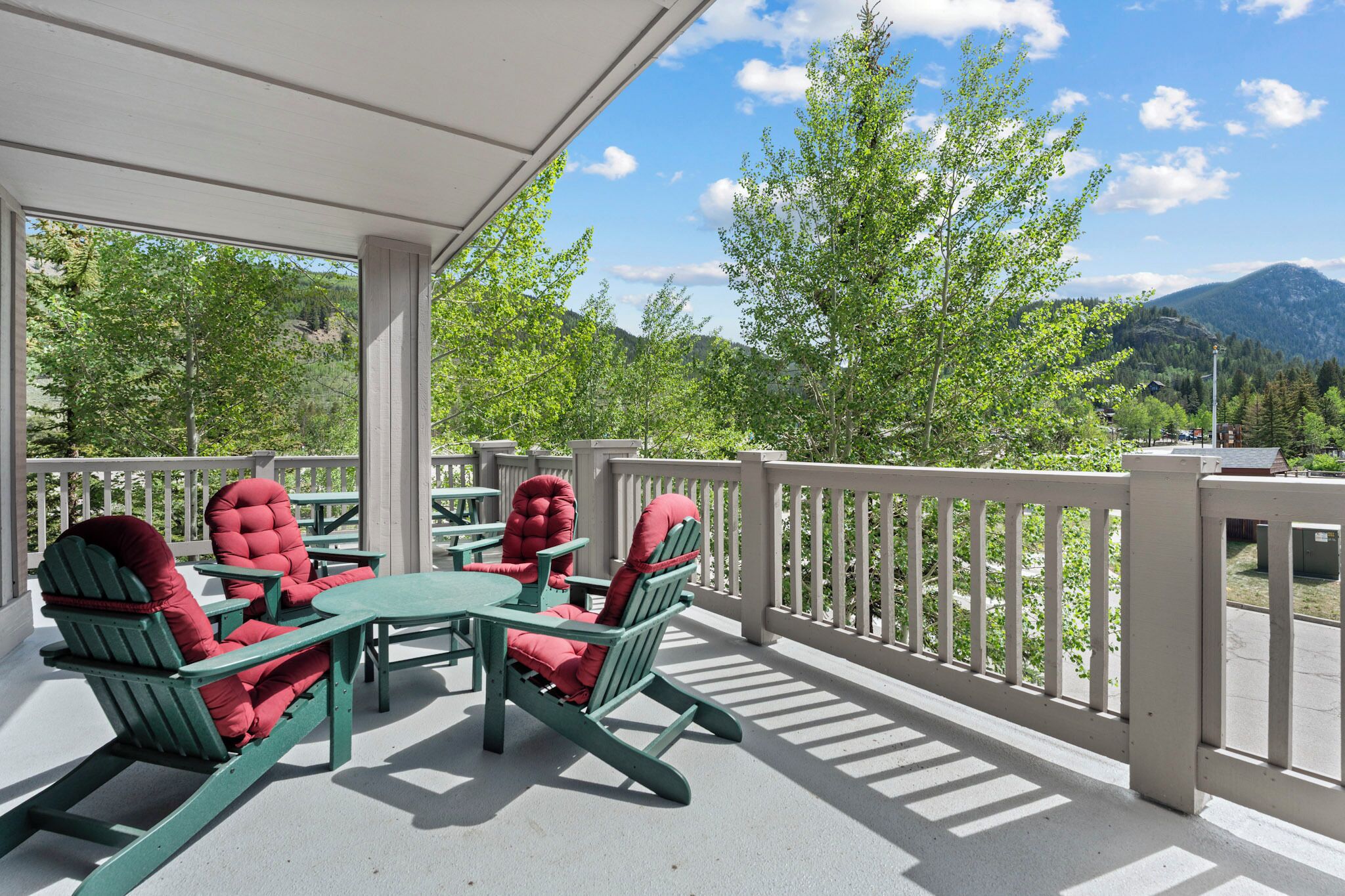 A covered outdoor seating area with Adirondack chairs and a table, overlooking a mountainous landscape.
