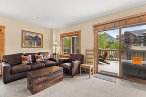 A living room with a sofa set, a wooden coffee table, a lamp, and a view of a mountain through a large sliding glass door. - Es8572-2 (Keystone)