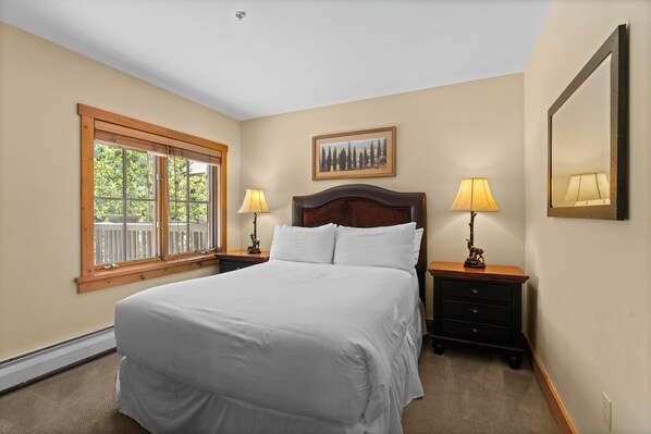 A hotel room with a large bed, two bedside tables with lamps, a window with a view, and a painting on the wall. - Es8572-2 (Keystone)