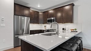 A modern kitchen with dark wooden cabinets, stainless steel appliances, and a white countertop. - Ctc3k3 (Keystone)