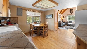 A kitchen with a dining table, chairs, and a ceiling fan. There is a window with a view of trees and a mounted animal head on the wall. - 68tlf2 (Frisco)