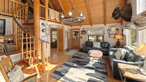A spacious living area with a wooden staircase, a chandelier, and a mounted animal head. - 68tlf2 (Frisco)