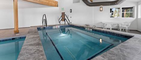 An indoor swimming pool with a wooden ceiling, a small seating area with chairs, and a window with a view.