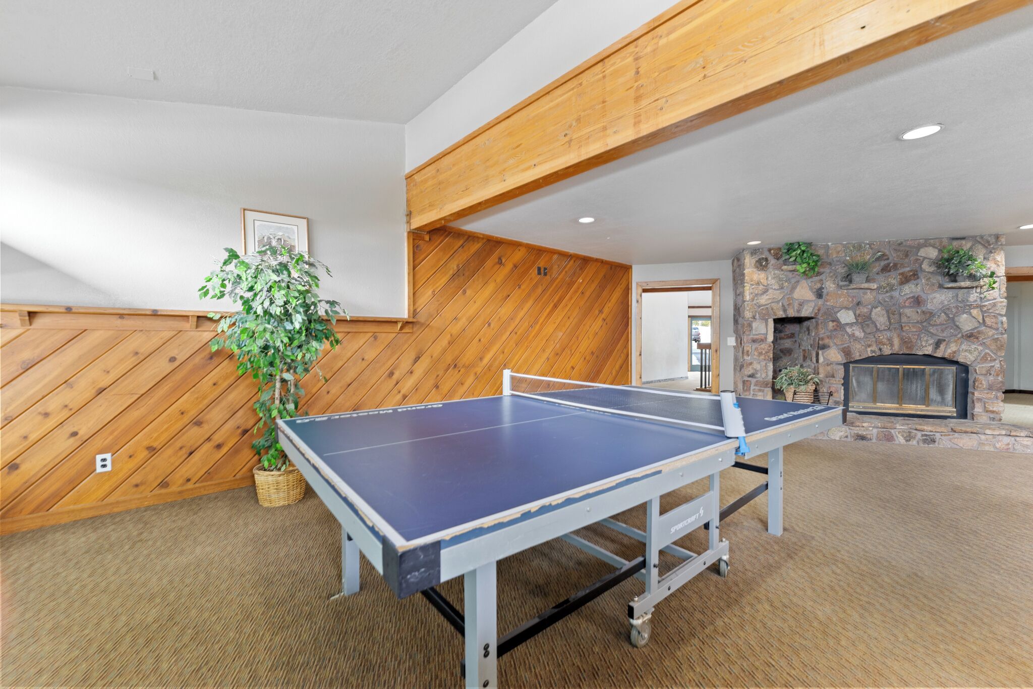 Mesa de ping pong en una habitación con paredes de madera y chimenea de piedra.