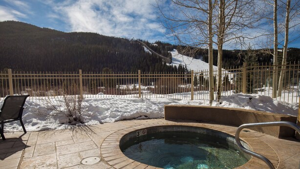 A hot tub with a stone surround, a wooden fence, and a chair in a snowy outdoor area with a mountain view. - Red Hawk Lodge #2212 (Keystone)