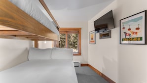 A bedroom with a bunk bed, a television mounted on the wall, and a window with a view of trees. - Red Hawk Lodge #2212 (Keystone)