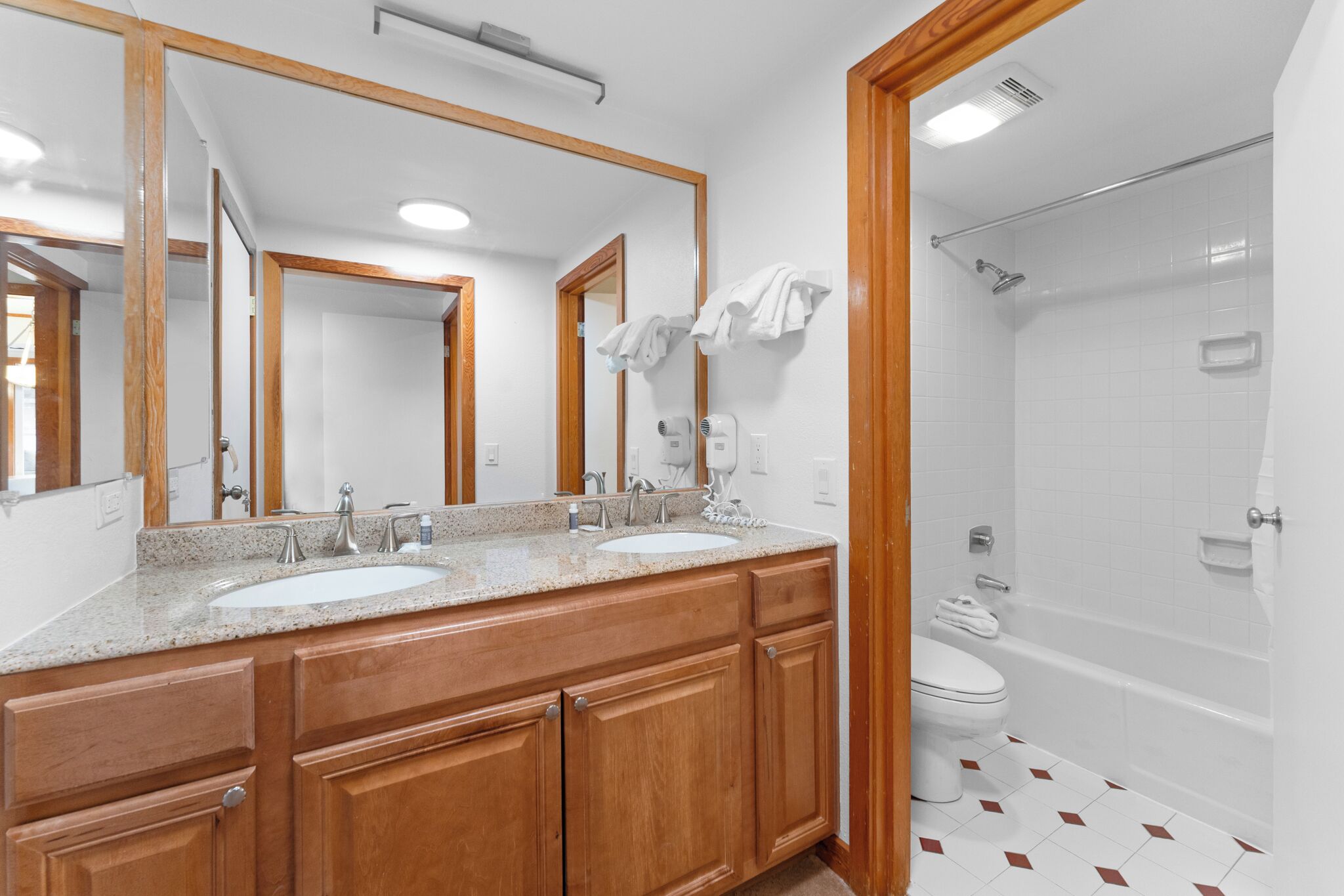 A bathroom with two sinks, a large mirror, a shower, and wooden cabinetry.