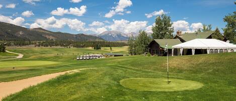 A golf course with a tent, a building, and mountains in the background.