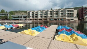A waterfront hotel with a dock filled with colorful paddle boats, a modern building with balconies, and a calm lake in the background. - Ls1476-0 (Keystone)