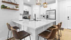 Una cocina moderna con una isla grande, taburetes de bar, luces colgantes y electrodomésticos integrados.